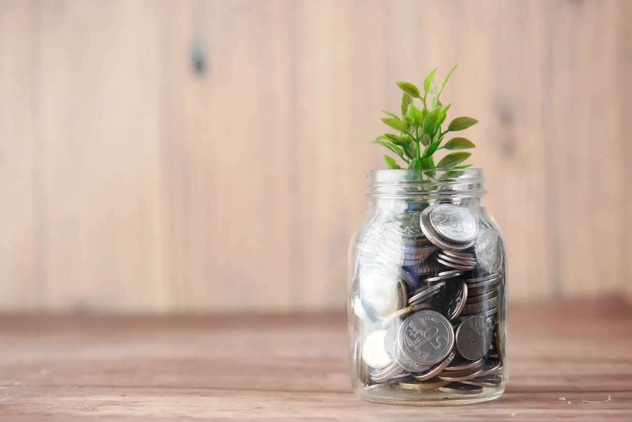 Mynt i en sparburk med en grön planta som växer, illustrerar skattefritt sparande på ISK upp till 300 000 kronor 2026